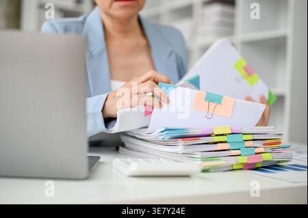 Senior Asian business woman checking documents sitting at table with laptop in office Stock Photo