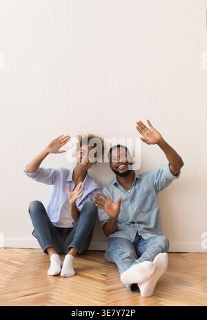 Cheerful Black couple talking and planning about interior design while sitting on floor against white wall in new home Stock Photo