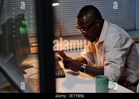 Focused Black male programmer in eyeglasses examining computer codes working overtime in office Stock Photo