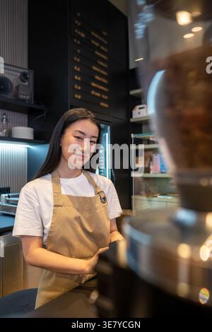 Smiling Asian female cafe worker standing at the counter in cafe Stock Photo
