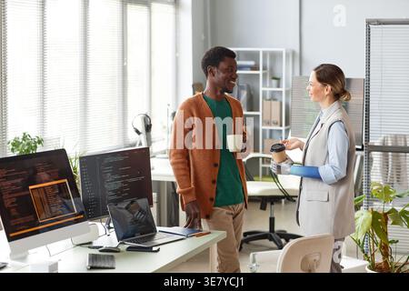Black male programmer holding coffee cup having conversation with disabled female colleague with bionic arm in office Stock Photo