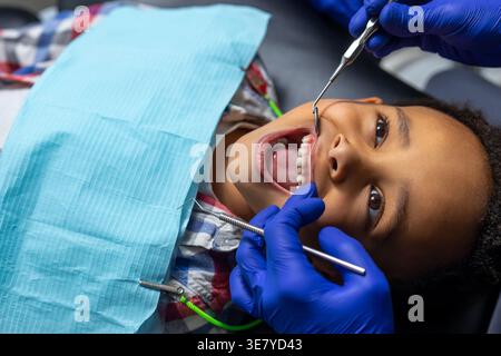 Black boy lying on bed having dental treatment with male dentist in clinic Stock Photo