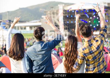 Chinese male and female friends raising arms making hand gestures having fun together while standing on concert ground at music festival Stock Photo