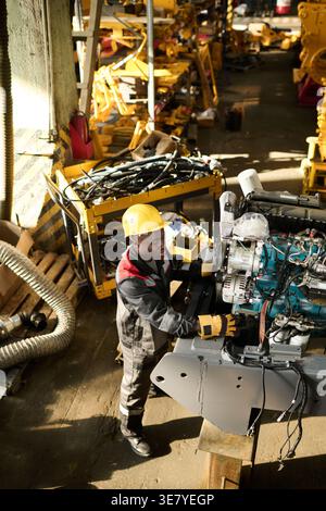 Black male factory worker in uniform wearing hardhat checking industrial machine while standing in workshop Stock Photo