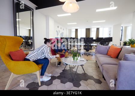 Middle Eastern male watching on tablet with caucasian female coworker sitting on sofa in office relaxation area during break Stock Photo