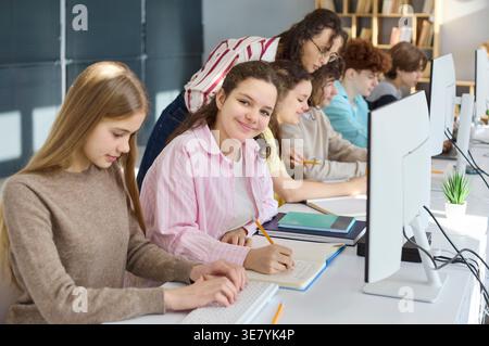 High school students coding at computers with teacher help in modern classroom Stock Photo