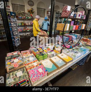 Two shoppers examine a variety of colorful stationery, notebooks, and gift boxes displayed on shelves and tables in a retail shop Stock Photo