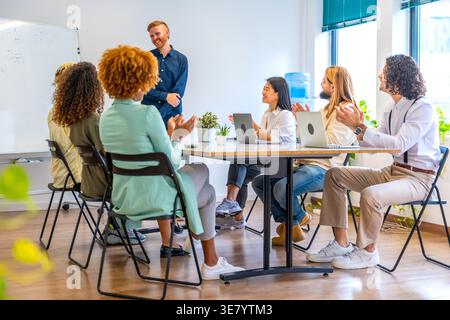 Smiling Asian business woman standing and being applauded by diverse colleagues during team meeting in the office Stock Photo