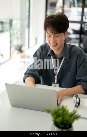Smiling Asian female office worker working on laptop sitting at desk in office Stock Photo