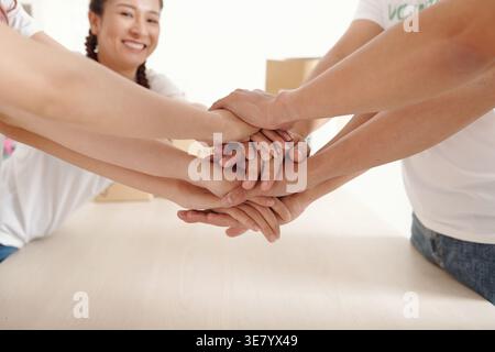 Group of Asian volunteers stacking hands in charitable center Stock Photo