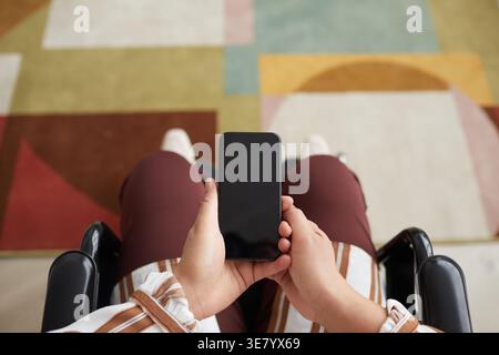 Hands of disabled mixed-race businesswoman in wheelchair and using smartphone in living room at home Stock Photo