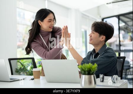 Asian male and female office workers giving high five to each other in office Stock Photo
