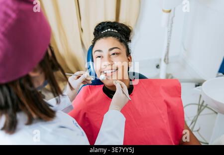Hispanic female dentist doing dental check up to Hispanic female patient lying on dental chair in clinic Stock Photo