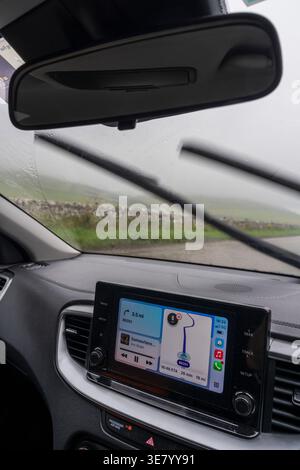 View from inside a car on a rainy day, showing windshield wipers in action and the navigation screen displaying a route Stock Photo