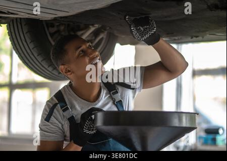 Smiling African American male car mechanic checking lifted vehicle  in auto repair shop Stock Photo