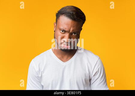 Frowning Black man in white shirt with a frowning face standing against yellow background in studio Stock Photo