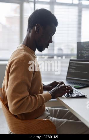 Black male programmer typing codes on computer sitting at table with laptop in office Stock Photo