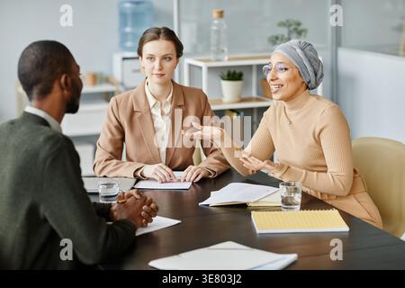 Mixed race and caucasian female HR managers discussing employment contract to mixed race male candidate during job interview in office Stock Photo