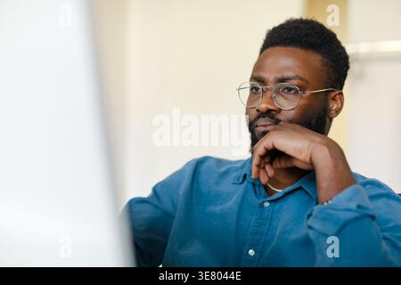Serious Black man wearing eyeglasses working on computer sitting at table in office Stock Photo