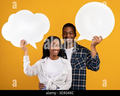 Black couple holding speech bubble cardboard while standing against yellow background in studio Stock Photo