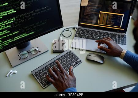 Black male programmer typing codes on computer while sitting at table with laptop in office Stock Photo