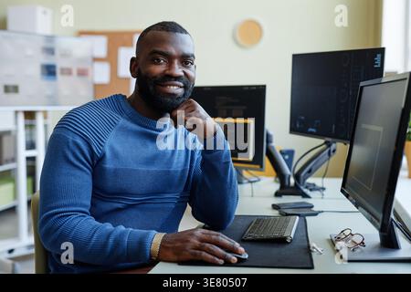 Black male programmer with hands under chin sitting at table with multiple computers in office Stock Photo