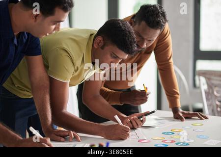Indian male UI and designers standing and leaning forward on table working on interface and icon for new mobile app in office Stock Photo