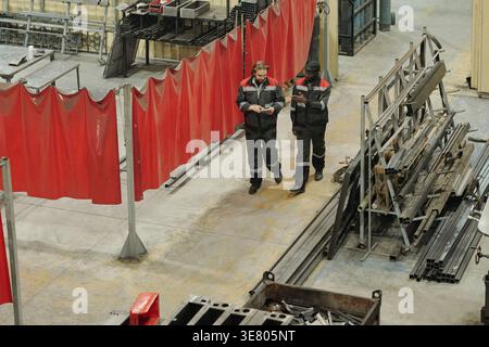 High angle view of Black and caucasian male workers making hand gesture and using tablet talking and walking along aisle of industrial plant Stock Photo