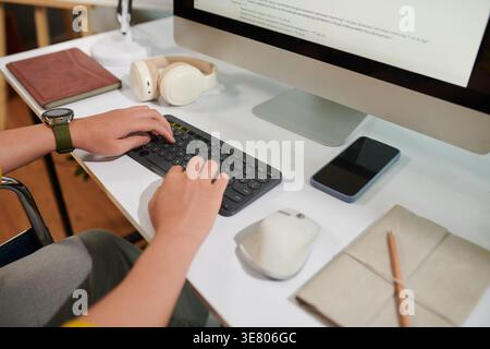 Asian man with disability working on computer sitting in wheelchair in office Stock Photo