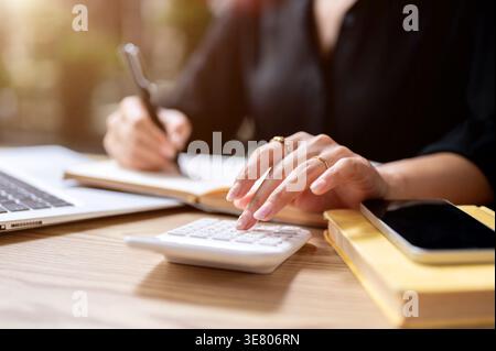 Close-up image of Thai woman's finger tapping on calculator while taking notes on table outdoor Stock Photo