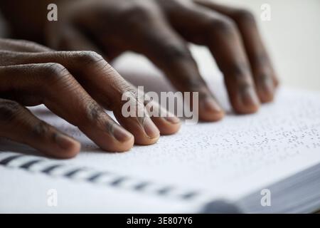 Close-up of hands of blind Black man reading book in braille over the wooden table indoors Stock Photo