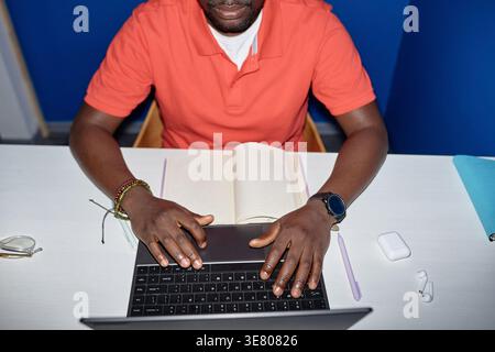 Cropped image of Black male office worker working on laptop sitting at desk in office Stock Photo