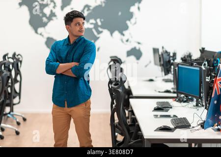 Middle Eastern businessman looking away while standing with crossed arms near computers in office Stock Photo