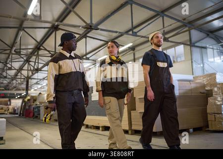Group of workers in uniform talking to each other while walking in warehouse Stock Photo