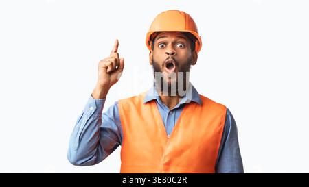 Black male worker wearing safety helmet pointing finger up while standing against white background in studio Stock Photo