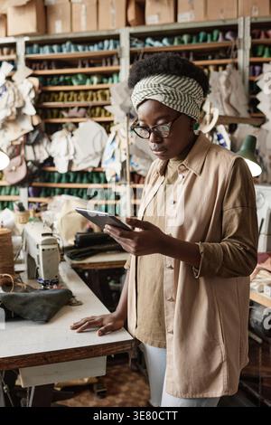 Black female designer wearing eyeglasses using tablet while standing at table in workshop Stock Photo