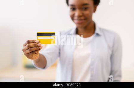 Smiling Black woman with short hair holding credit card standing in kitchen at home Stock Photo