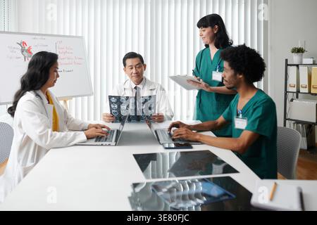Diverse group of medical professionals sitting at table looking at x-ray result in conference room at hospital Stock Photo