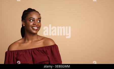 Surprised Black woman looking sideways standing against beige background in studio Stock Photo