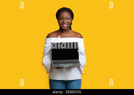 Black woman showing laptop standing against yellow background Stock Photo