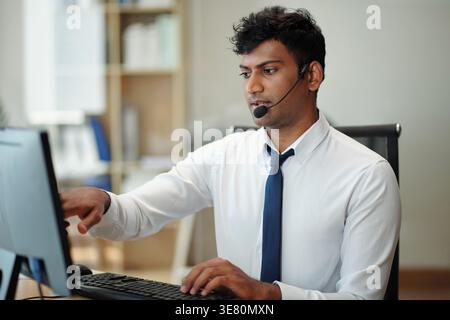Indian manager with headset sitting at table working on surveillance computer in security room Stock Photo