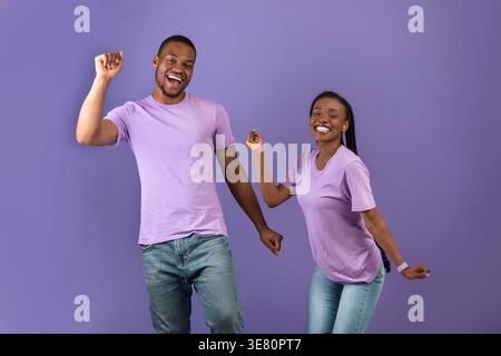 Smiling Black couple dancing together against purple background in studio Stock Photo