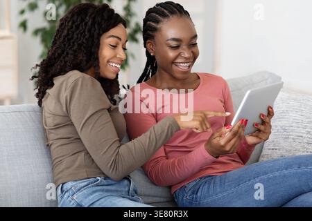 Black female friends using tablet together while sitting on sofa in living room at home Stock Photo