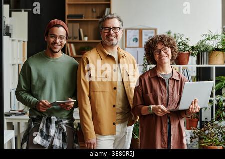 Group of IT specialists standing together holding digital gadgets in office workplace Stock Photo