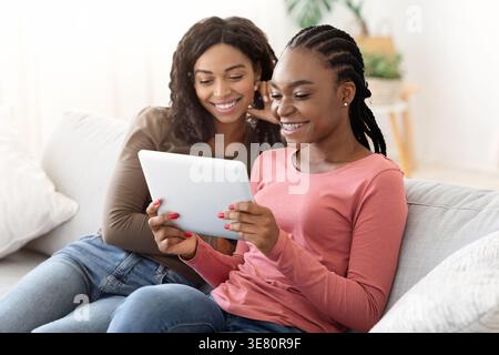 Black female friends using tablet together while sitting on sofa in living room at home Stock Photo