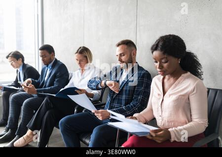 Caucasian businessman holding documengt looking at watch sitting with colleagues in sofa at the office Stock Photo