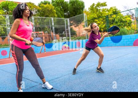 Diverse of female friends playing pickleball together in outdoor court during daytime Stock Photo