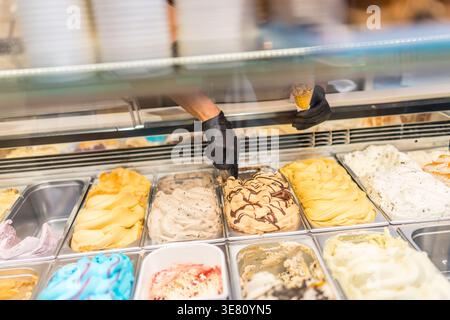 Hands of male worker wearing gloves holding cone and scooping ice cream from the counter in the store Stock Photo
