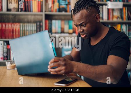 Black man with dreadlocks holding laptop sitting at table in cafe Stock Photo