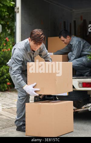 Asian delivery men unloading cardboard boxes from truck outdoors during daytime Stock Photo